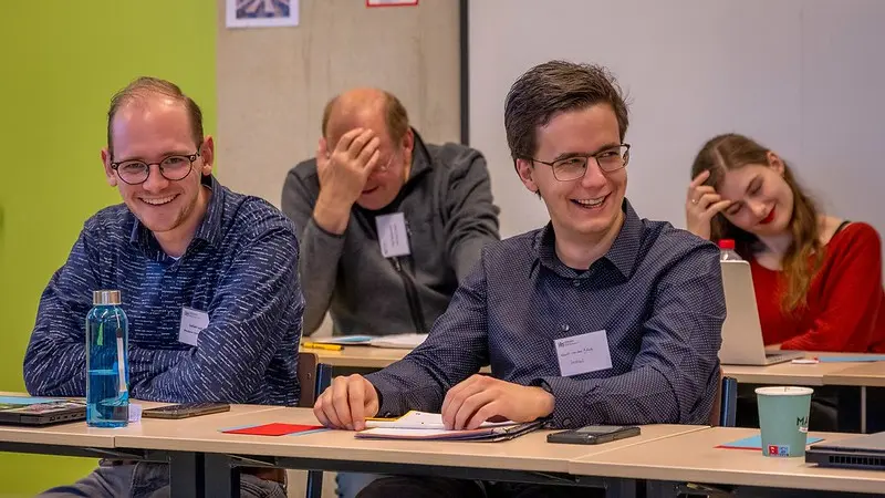 Foto van de i&i-conferentie: vier aanwezigen zitten aan tafels en moeten lachen om iets dat is gezegd